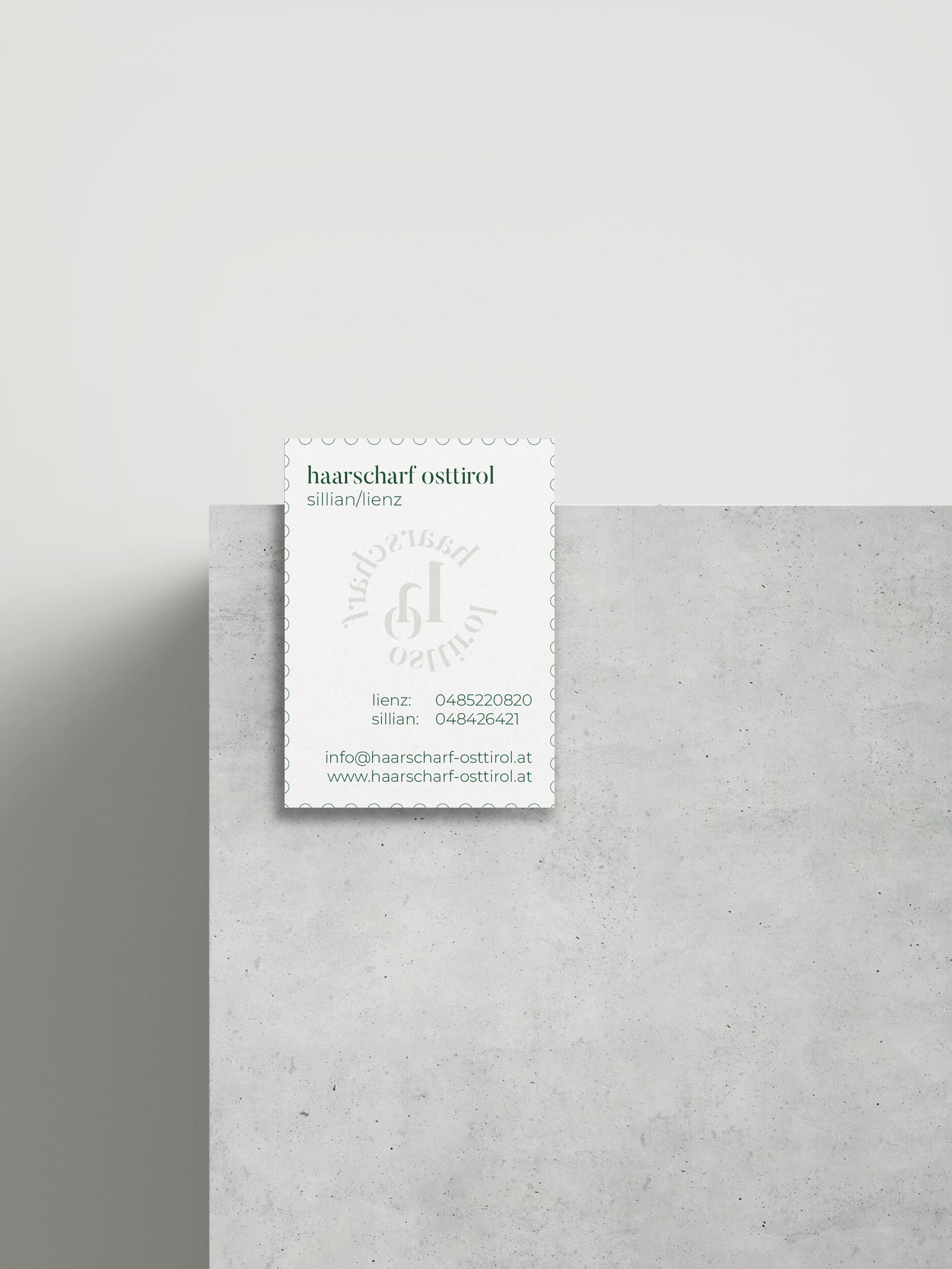 Nahaufnahmen von einer weißen Visitenkarte mit den Haarscharf Osttirol Kontaktinformationen auf einer Betonkante mit weißem Hintergrund und harten Schatten