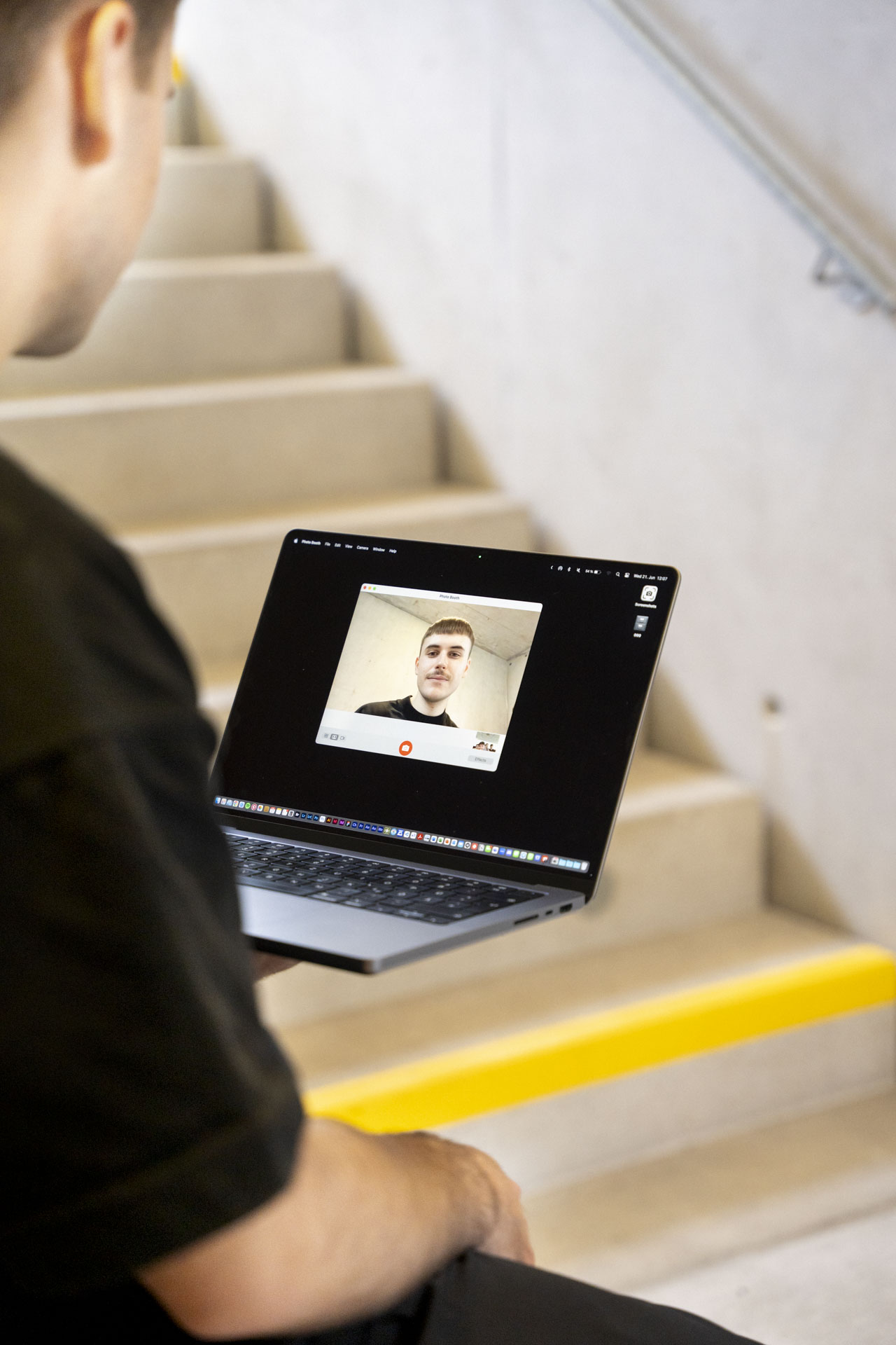 Bastian Gasser haltet den Laptop mit einer Hand und am Display sieht man ihn selbst über die live Webcamaufnahme
