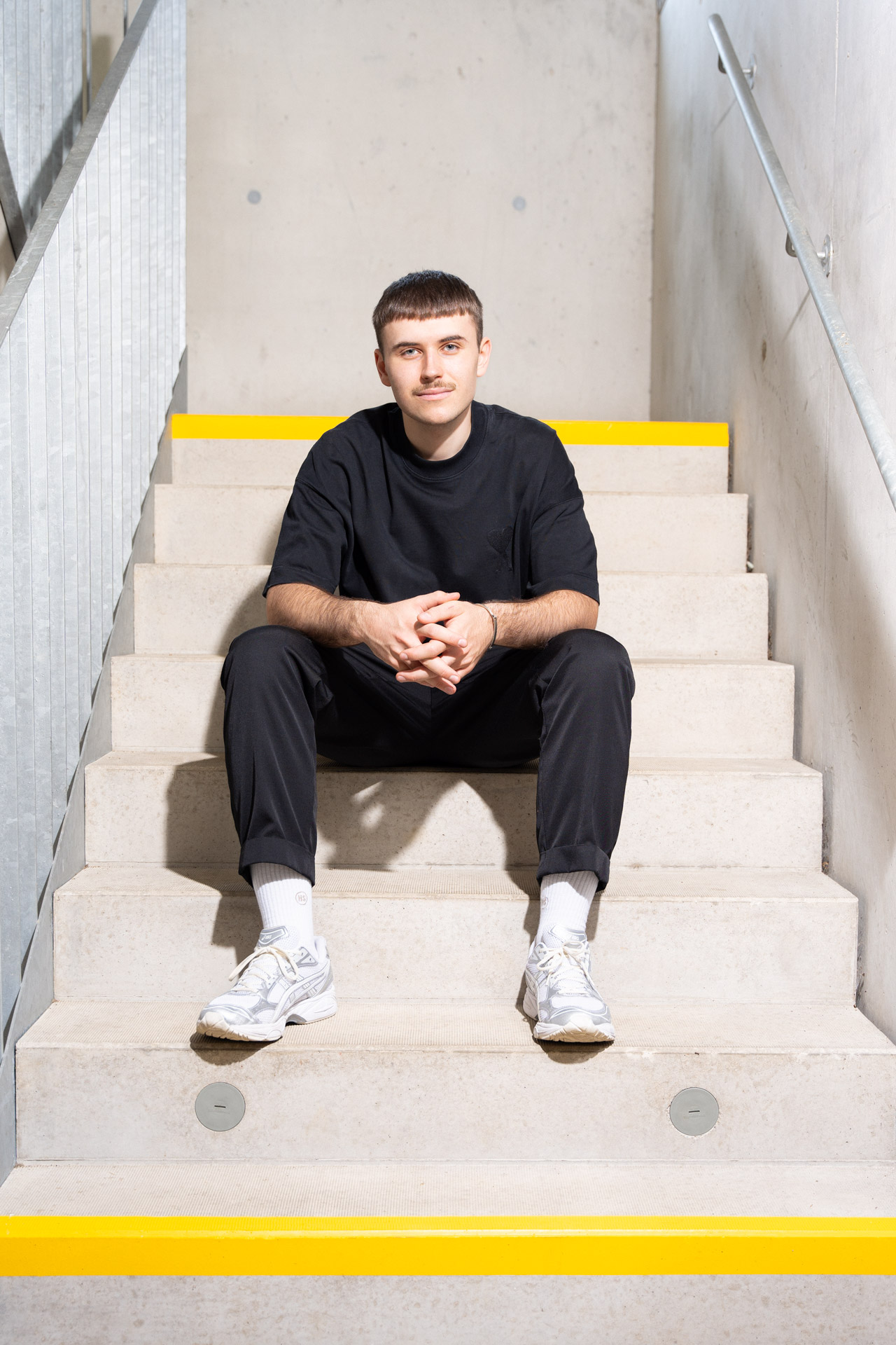 Portrait von Johannes Handlechner sitzend auf einer Betonstiege mit einem Eisengeländer